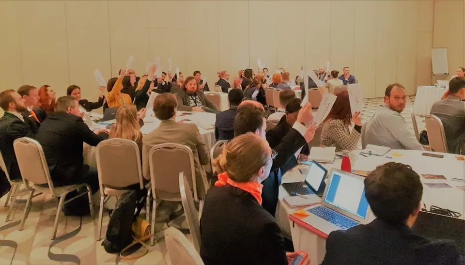 National Presidents raising their hands to vote at tables in a meeting room during the first 2020 Assembly