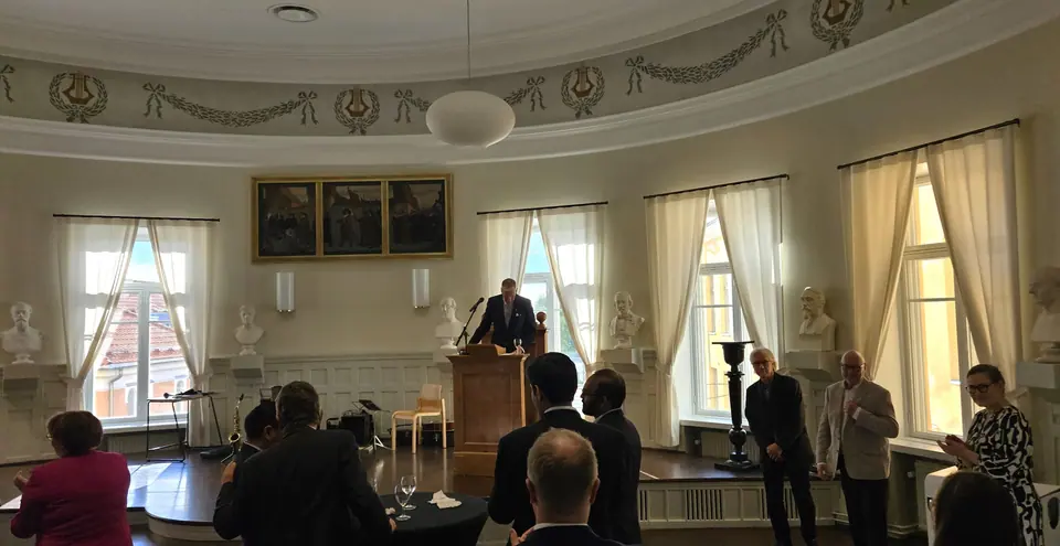 Officials at a reception in a historic hall with tall windows