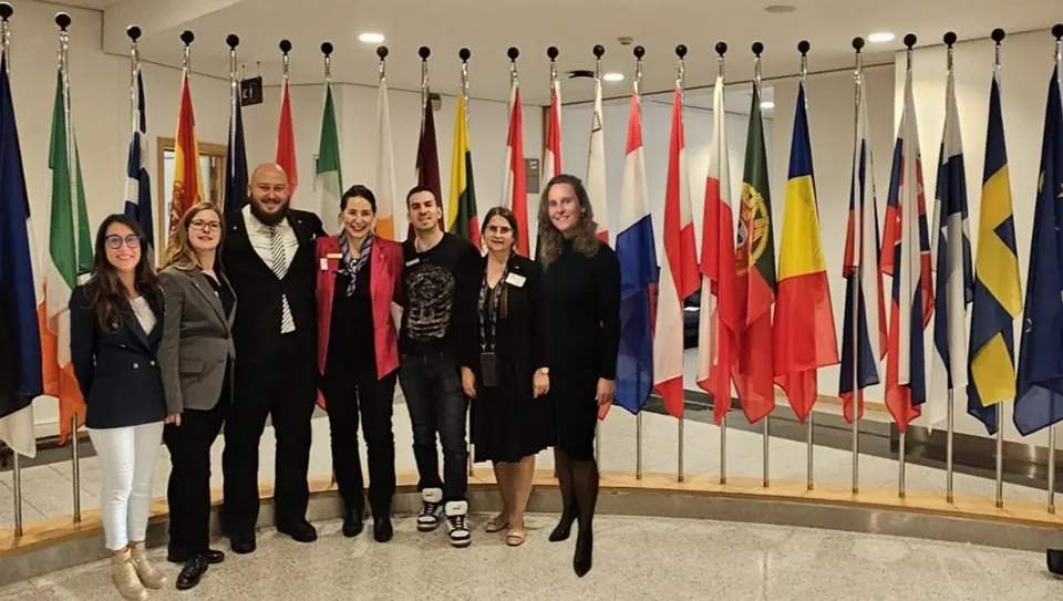 The organiser team standing in front of the row of EU member state flags in the European Parliament