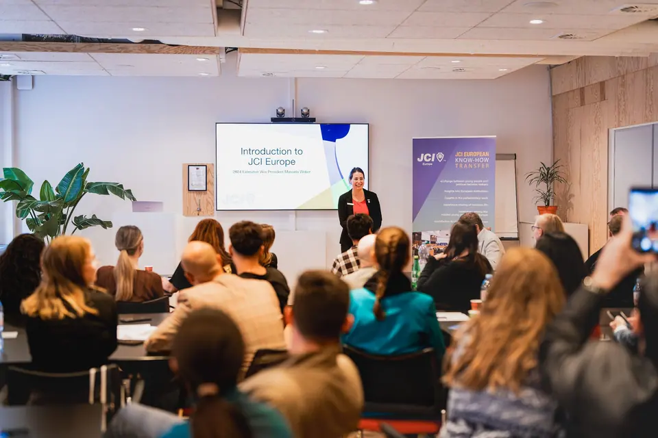 A presenter introducing JCI Europe on a screen in a seminar room with participants seated at tables