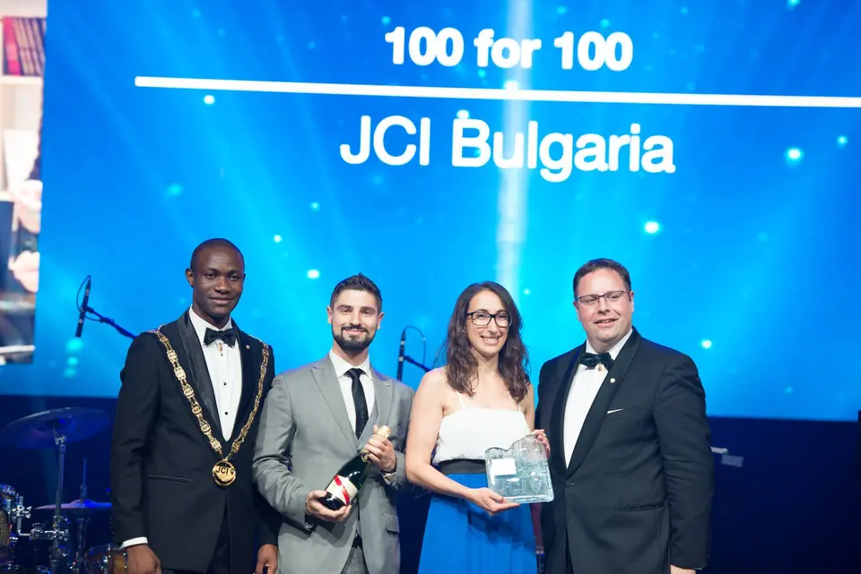 Four people on stage receiving an award in front of a screen reading 100 for 100 JCI Bulgaria