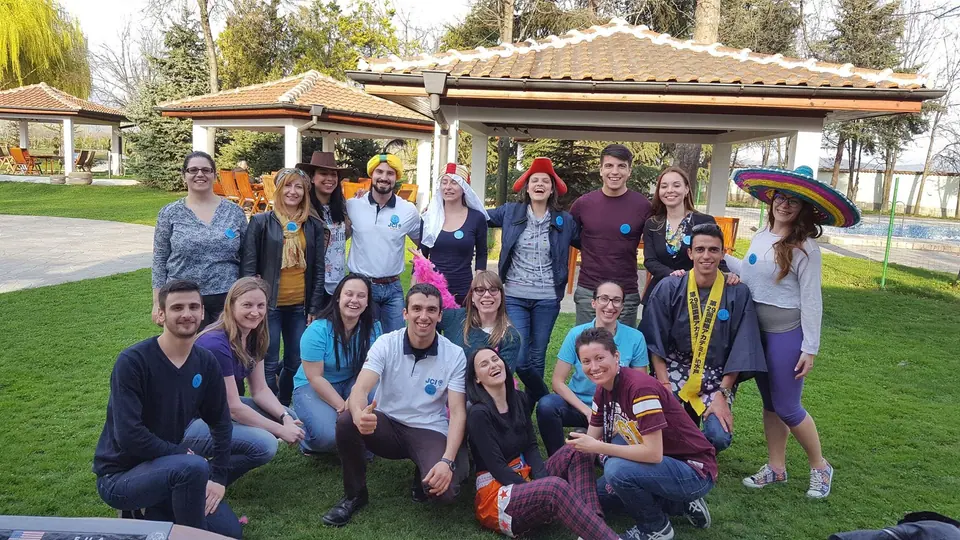 A JCI Bulgaria team-building group in a garden, some wearing funny hats