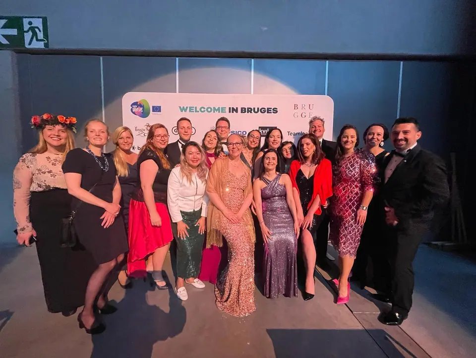 The JCI Europe team in evening wear on stage in front of a Welcome in Bruges backdrop