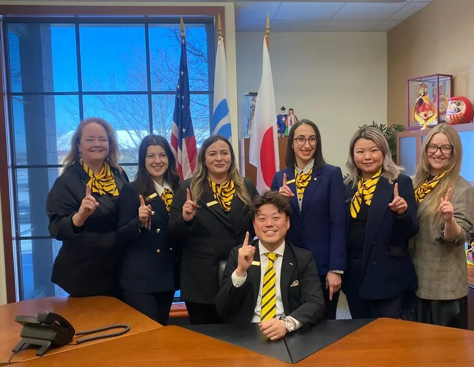 The 2025 JCI Europe Board of Directors in yellow scarves posing with 2025 JCI President Keisuke Shimoyamada at a table