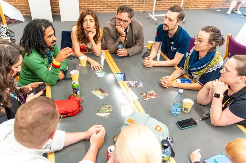 Participants seated around a table at a JCI European Conference workshop, talking and laughing