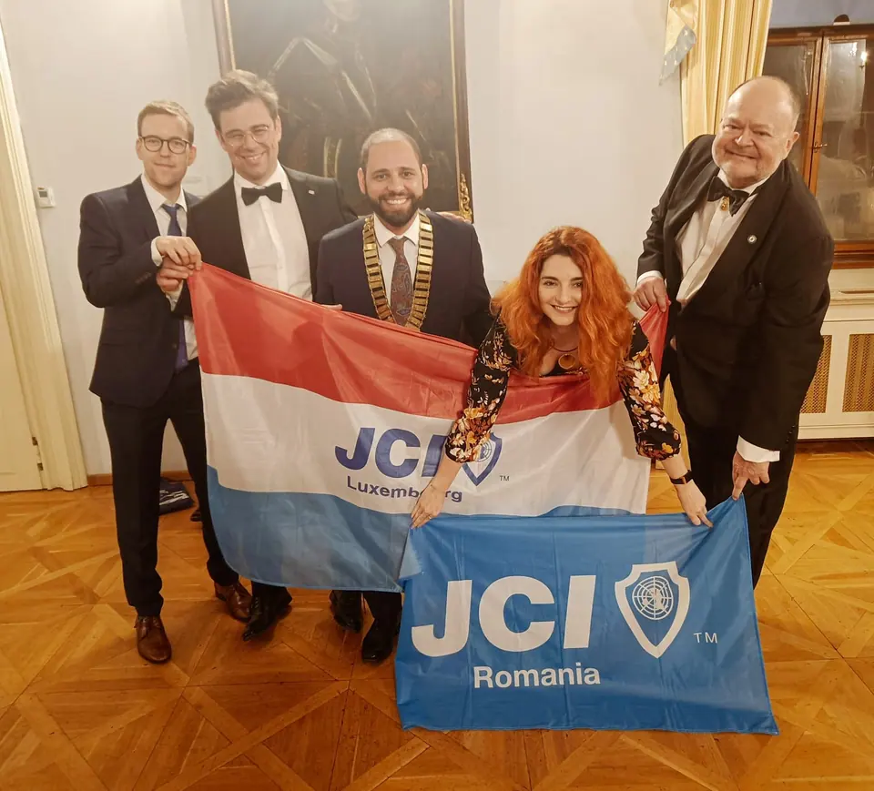 Five people in formal wear holding a Luxembourg flag and a JCI Romania flag