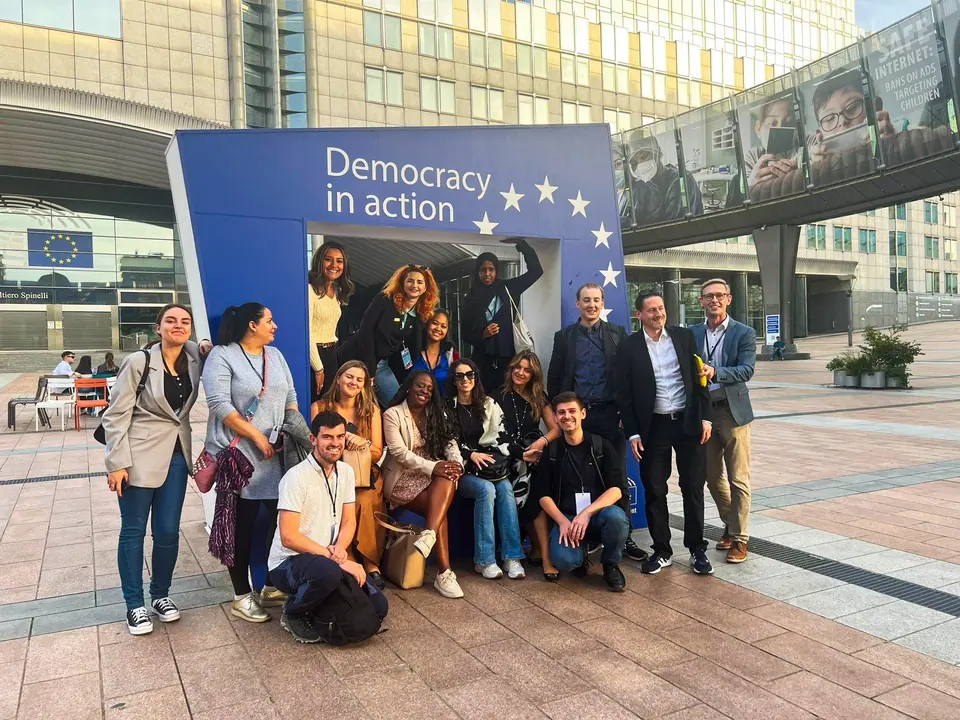 A group posing in front of a Democracy in action sign outside the European Parliament