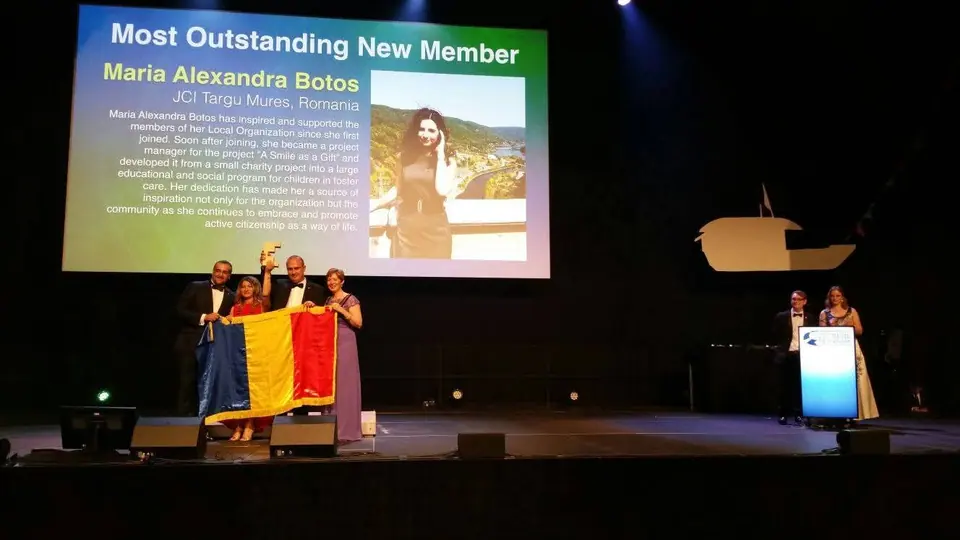 A stage with Romanian flags and a screen announcing Most Outstanding New Member, Maria Alexandra Botos