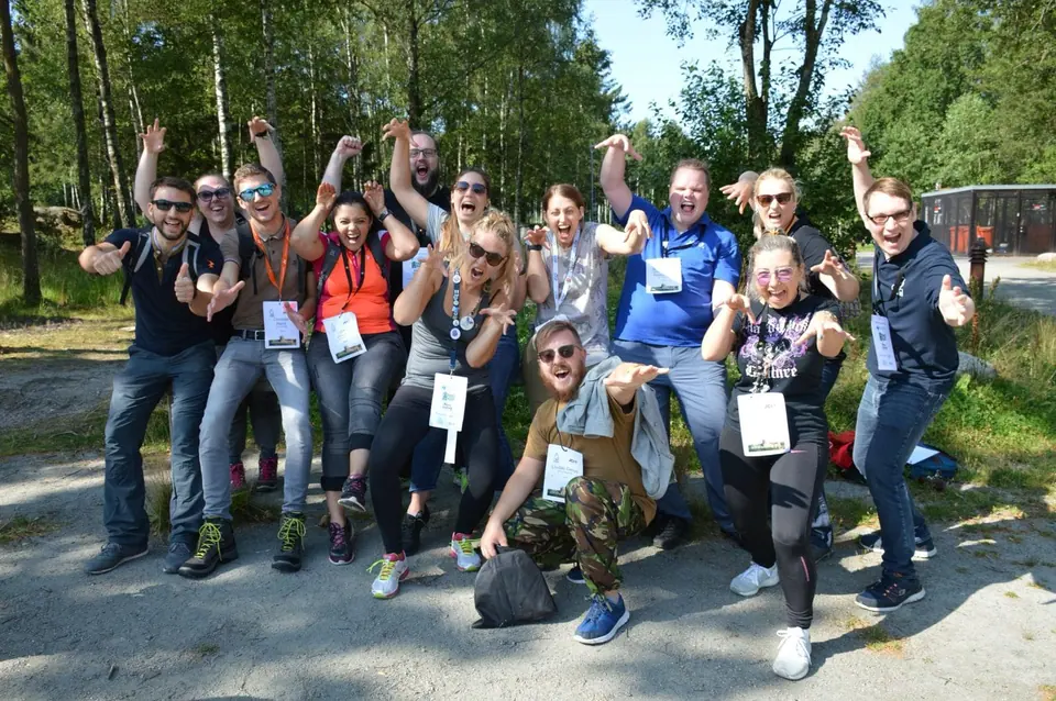 Group of European Academy participants posing and cheering in a sunny forest clearing