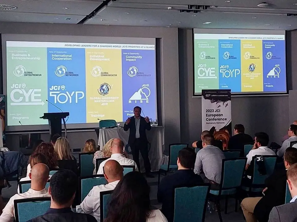 A presenter in front of two screens showing the four areas of opportunity of JCI, with the CYE and TOYP logos