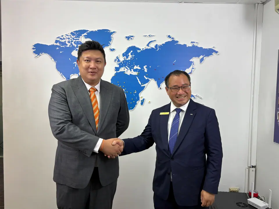 Two men in suits shaking hands in front of a blue world map on a white wall