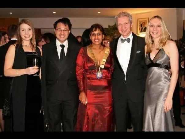 Five people in evening wear at a gala dinner, one wearing a chain of office