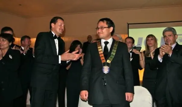 Men in tuxedos applauding a man in a chain of office at a gala evening