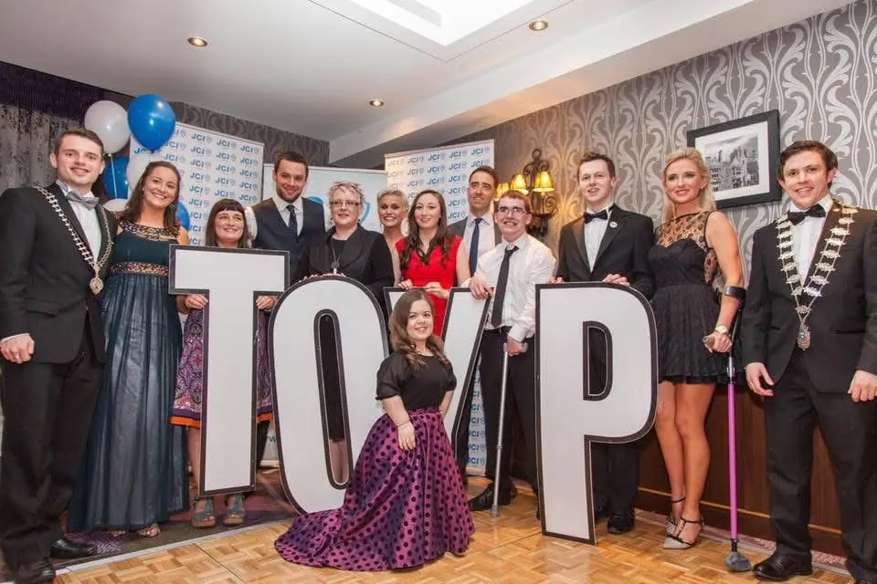 A group posing behind large letters spelling TOYP, with several wearing chains of office