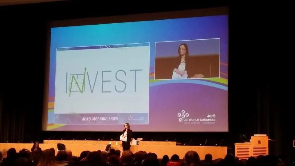 A speaker on a stage in front of a screen reading INVEST at a JCI World Congress