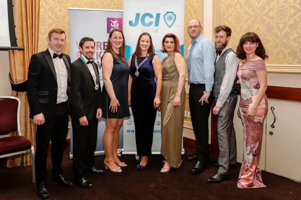 Seven people in formal wear in front of a JCI banner at an event
