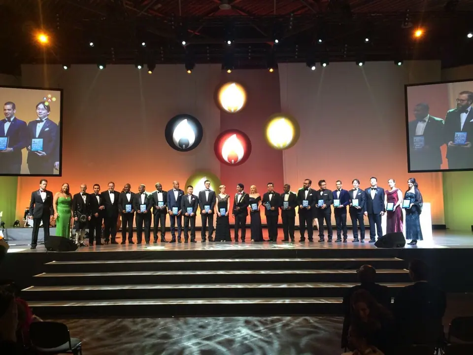 A large group in formal wear lined up on a lit stage at a gala