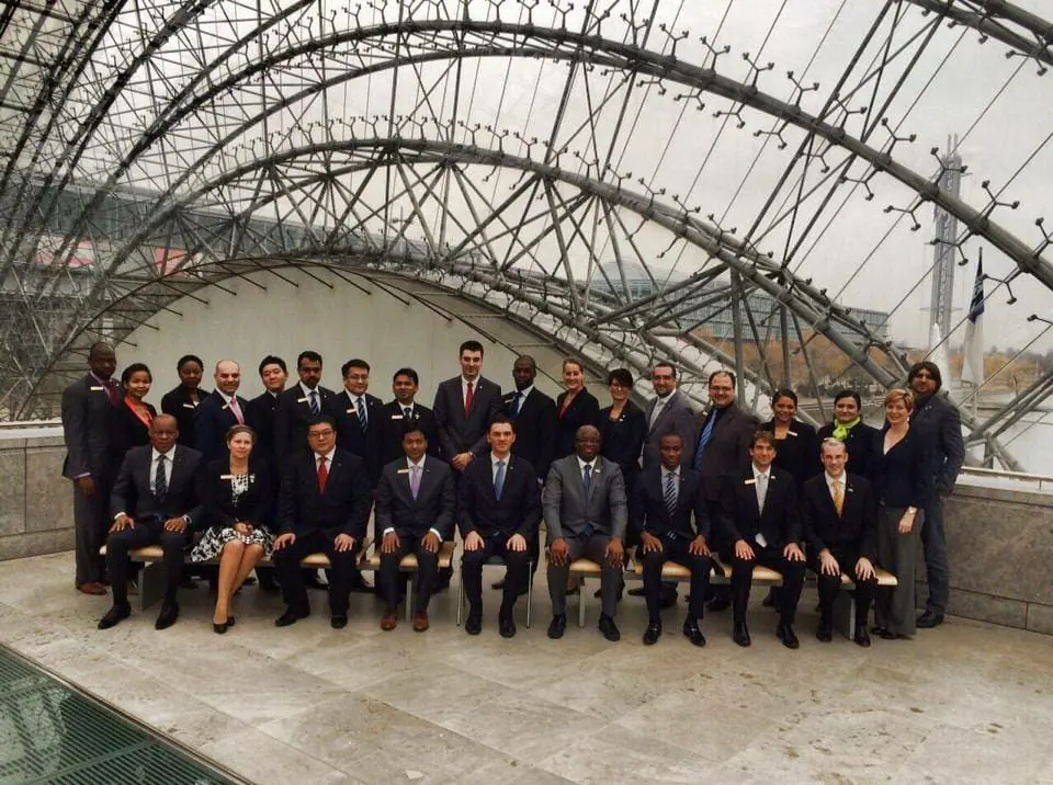 A group of about thirty people in formal wear posing under a glass and steel roof