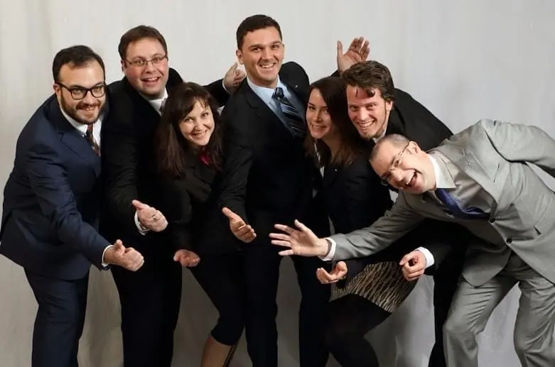 Six people in smart clothes posing playfully in front of a grey backdrop