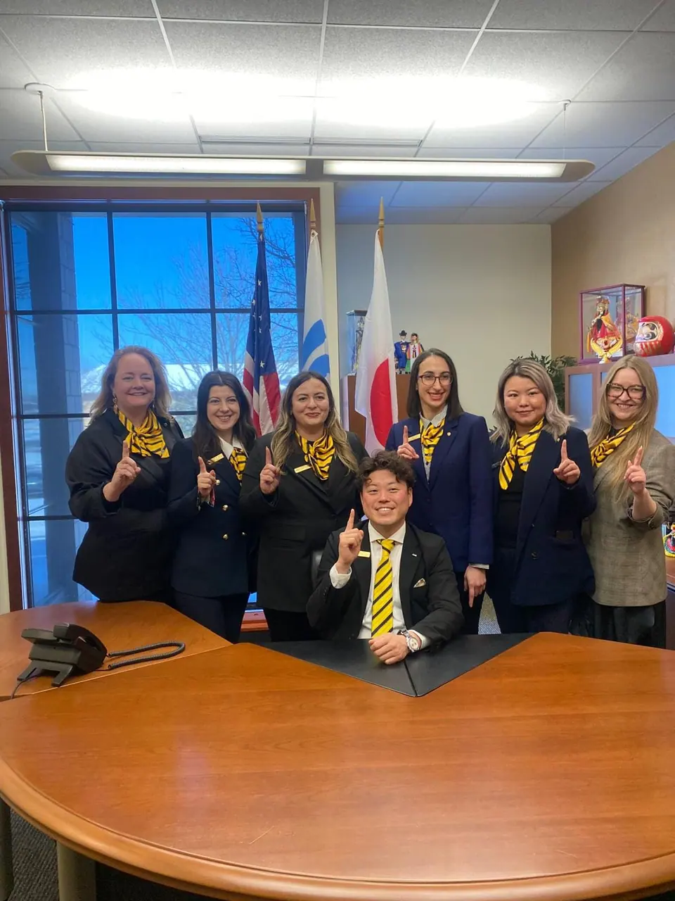 The 2025 JCI Europe board in yellow scarves posing around a curved wooden table with the 2025 JCI President