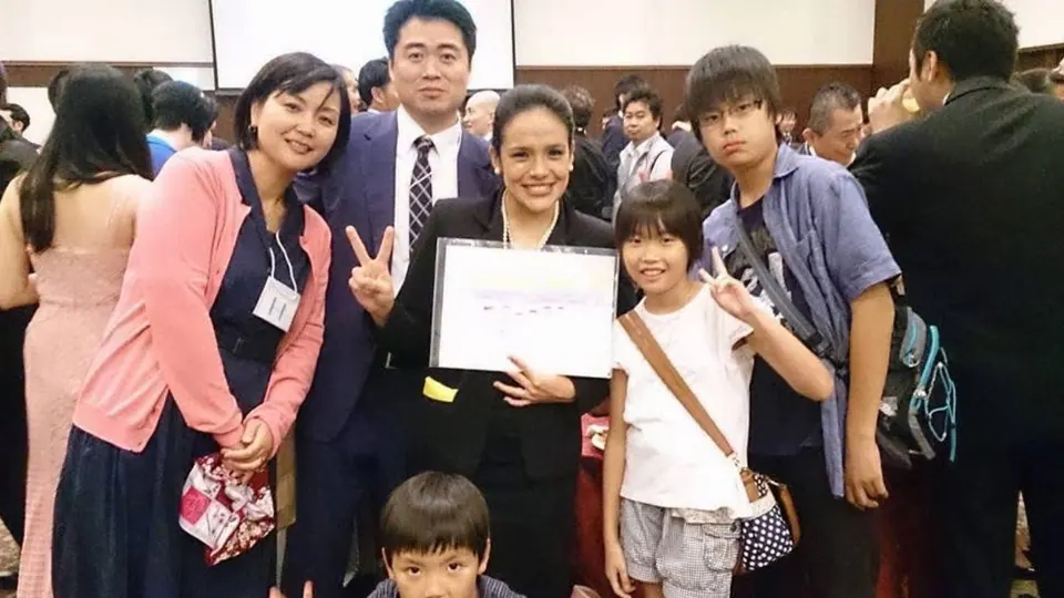 Alejandra Castillo holding a certificate, surrounded by smiling Japanese friends and families