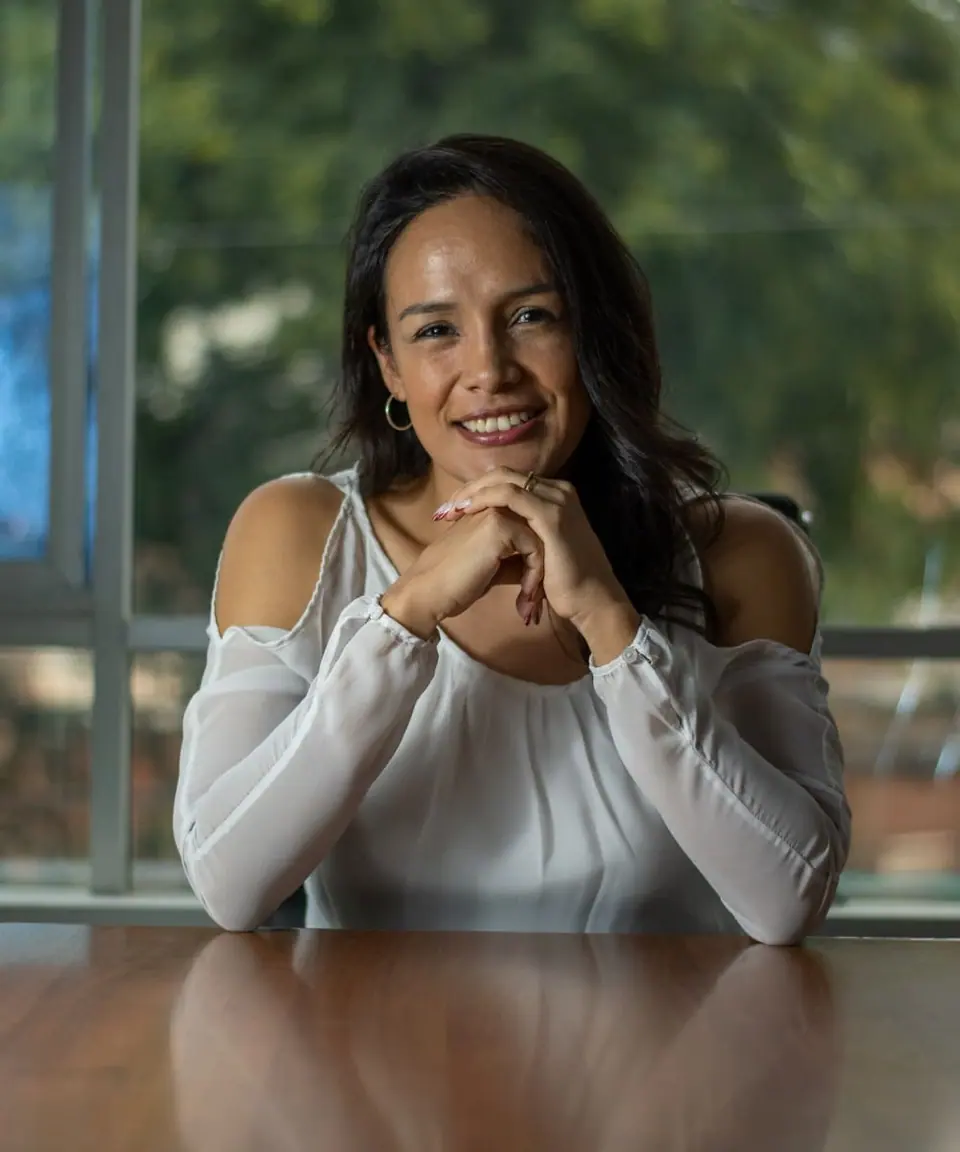 Alejandra Castillo smiling with her hands clasped under her chin at a wooden table
