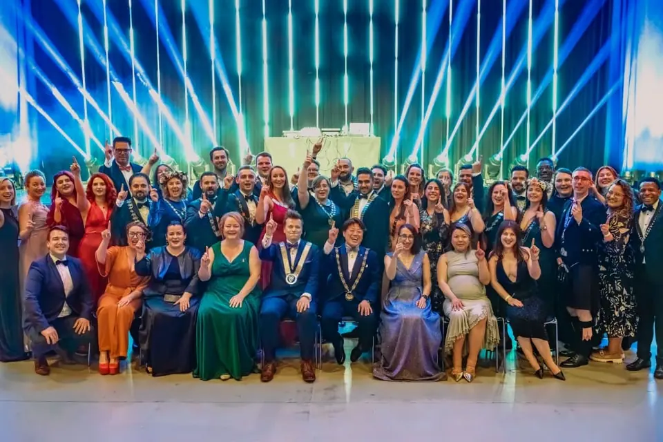 A large group in evening wear posing on stage under a blue and green light show at a gala