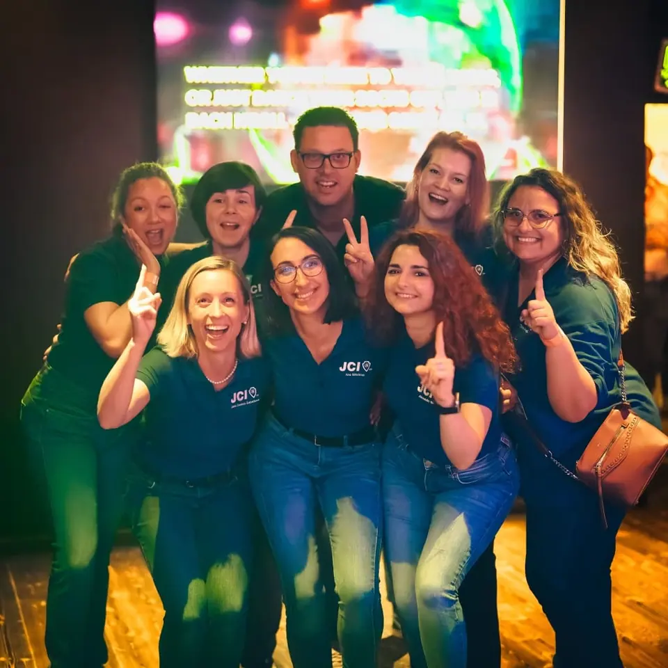 Six JCI members in dark green T-shirts laughing and making the JCI hand sign