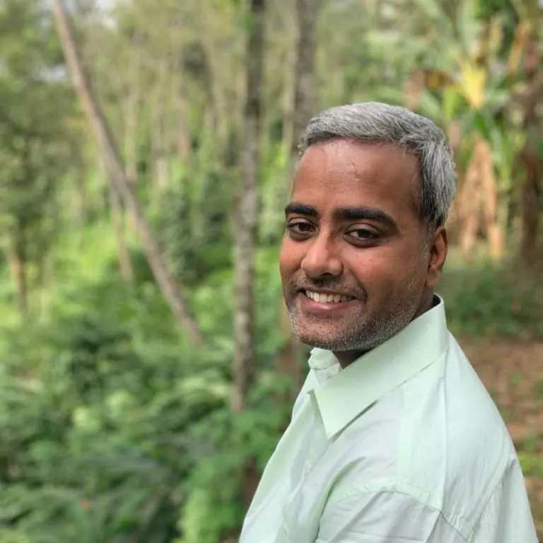 Portrait of Ullas Marar, smiling, in a light green shirt in front of trees