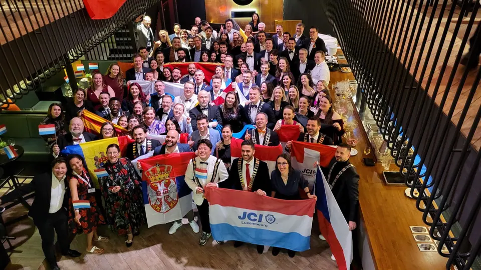 A large group of National Presidents holding national flags, seen from a staircase above, at a JCI Europe meeting