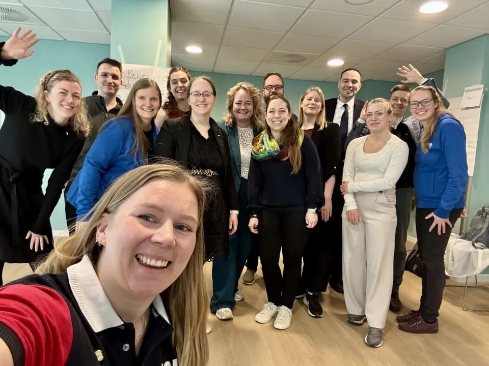 A group selfie of about twenty people in a bright meeting room
