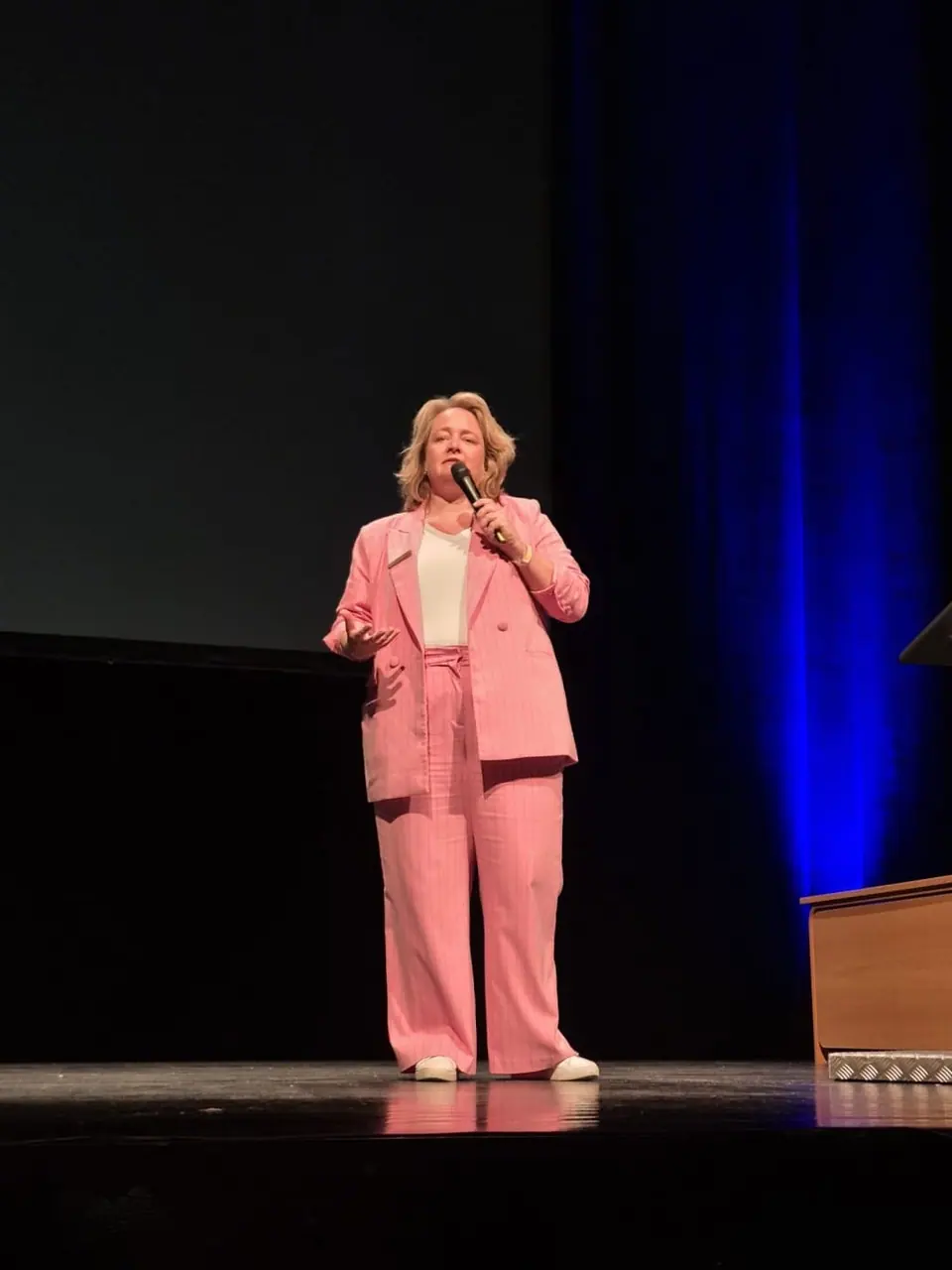 A woman in a pink suit speaking on a dark stage