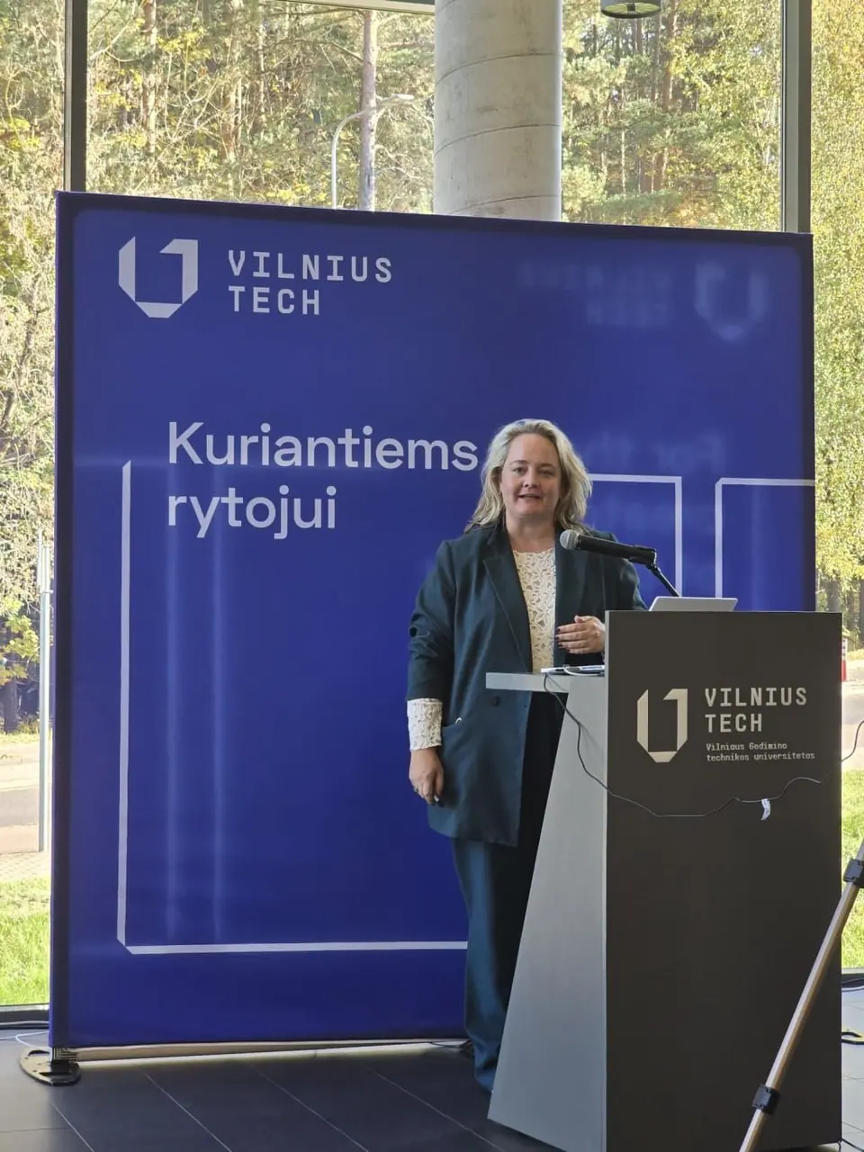 A woman speaking at a lectern in front of a Vilnius Tech banner