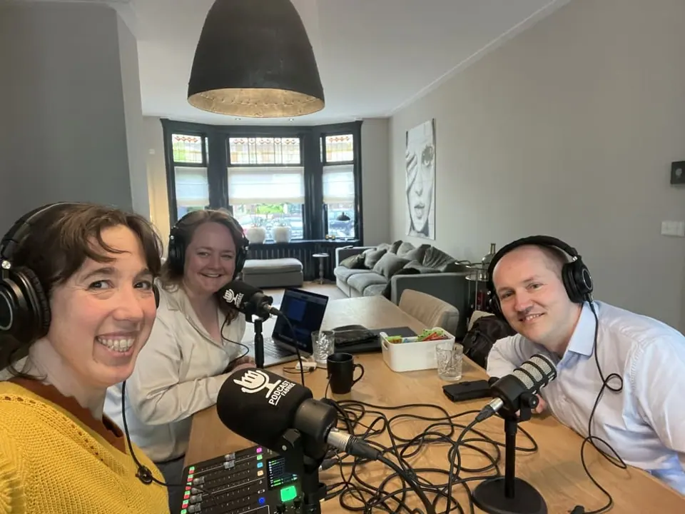 Three people wearing headphones recording a podcast around a table