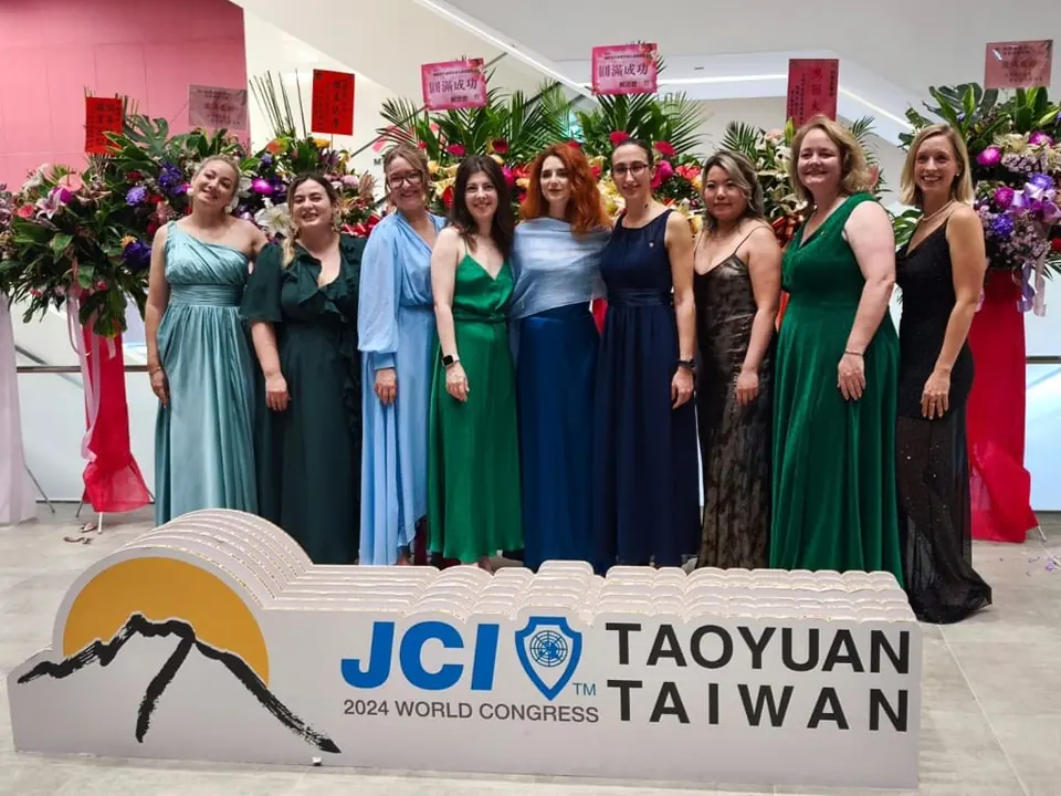 Eleven women in evening gowns standing behind a JCI Taoyuan, Taiwan 2024 World Congress sign