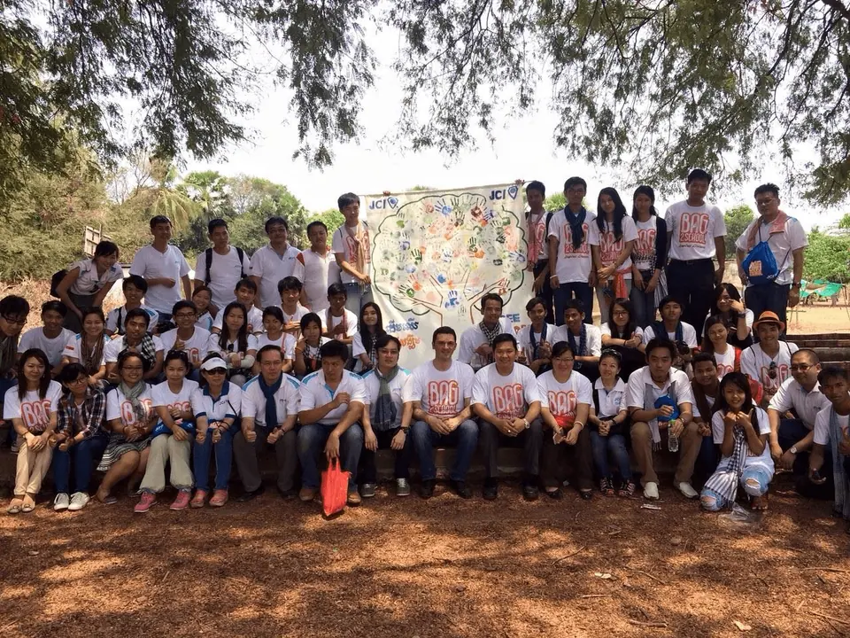 A large crowd of schoolchildren and volunteers in white T-shirts posing outdoors under trees