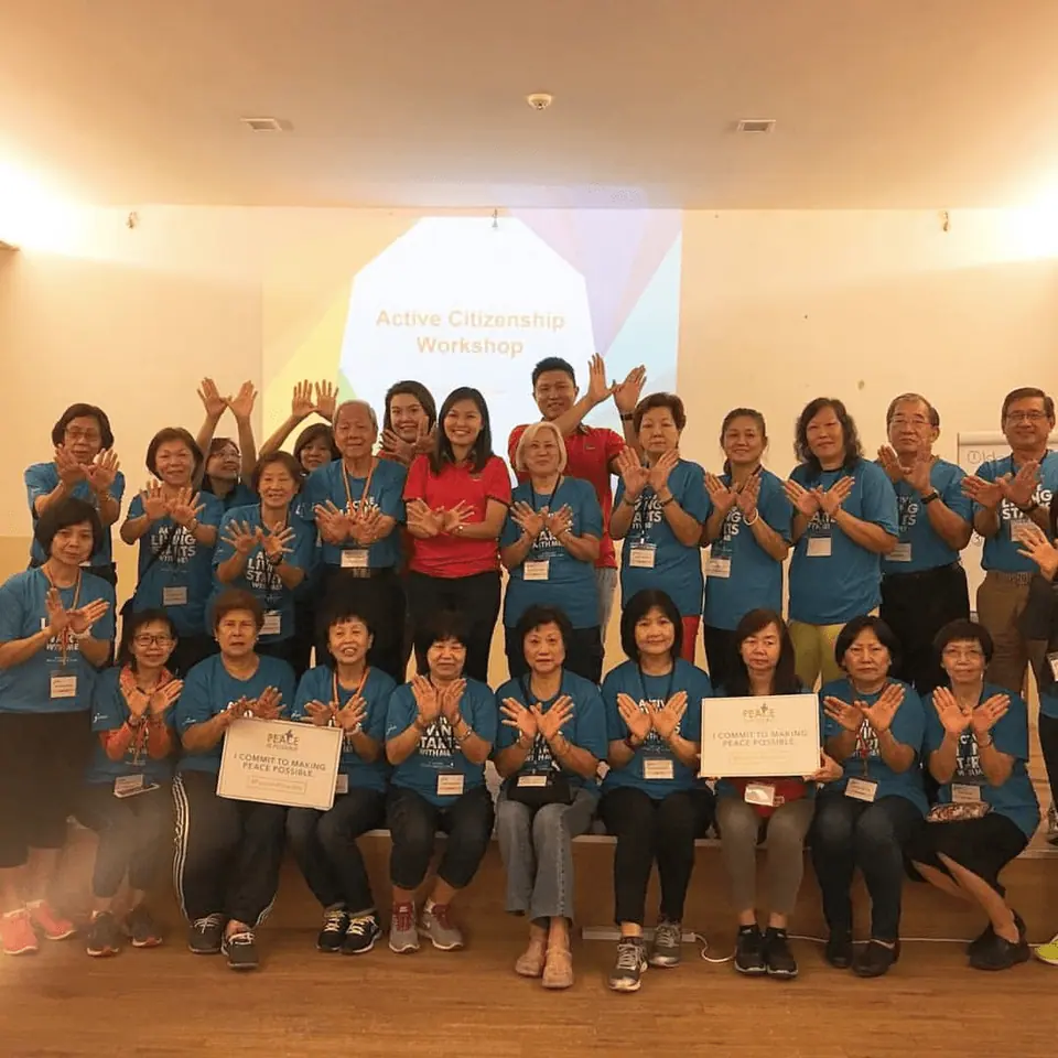 A group in blue T-shirts clapping, with two members holding certificates, at a workshop