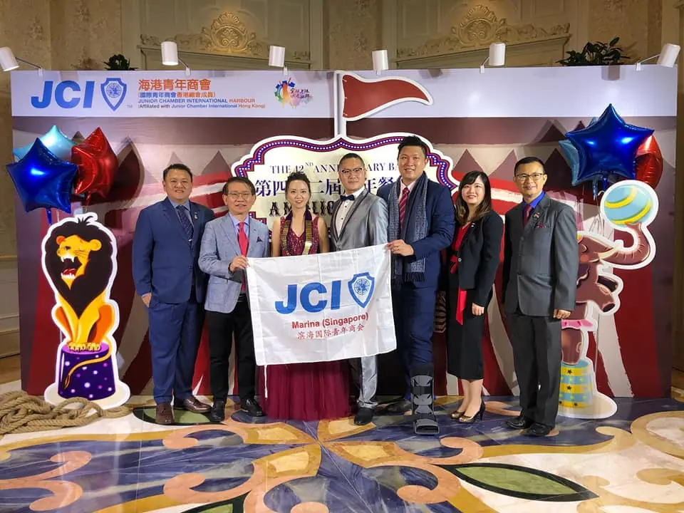 Members standing around a JCI banner in front of anniversary decorations with a lion figure