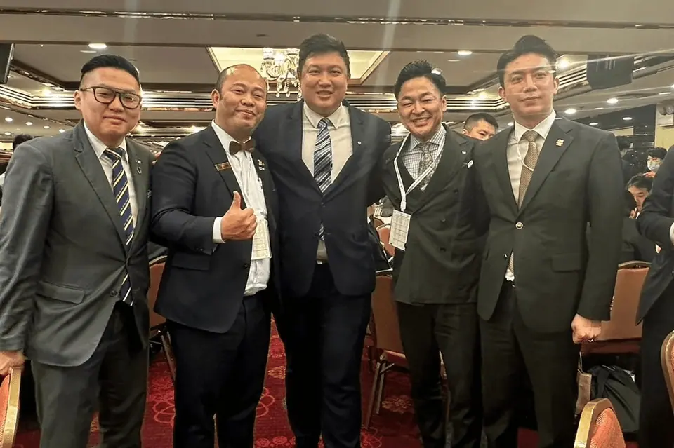 Five men in suits posing together at an indoor reception