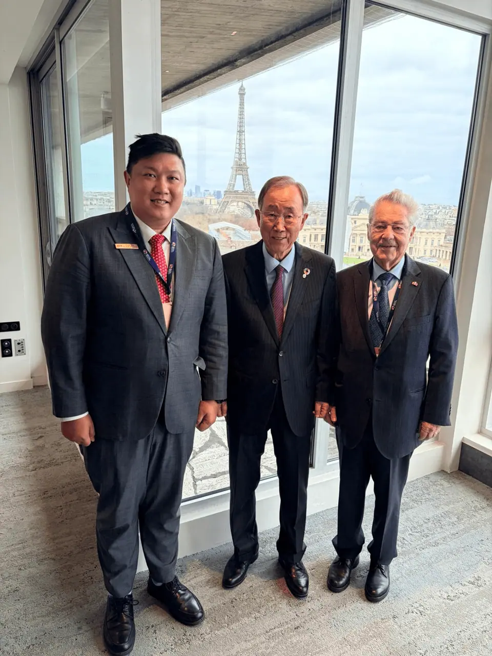Three men in suits standing together in front of a window overlooking a city