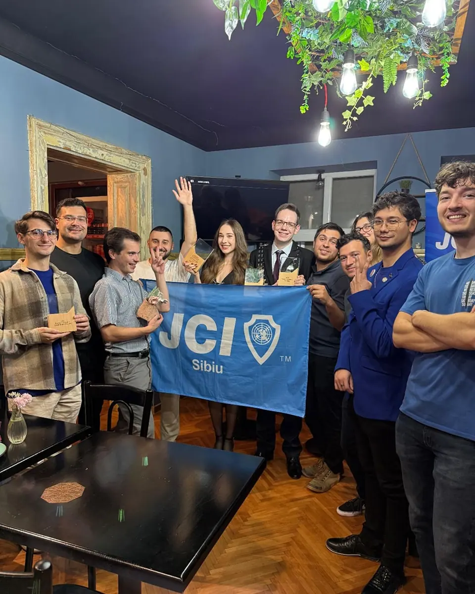 Members of JCI Sibiu holding up their blue JCI Sibiu flag in a café
