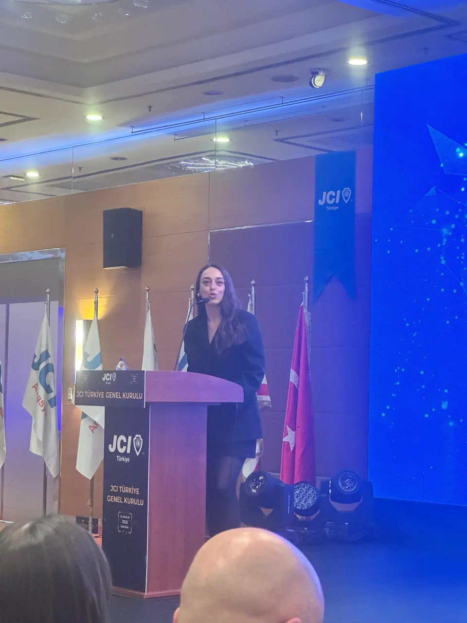 A woman speaking at a JCI lectern on a blue-lit stage