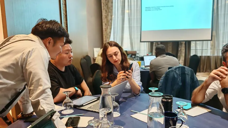Participants working at a table during a training session, with a presentation on a screen behind them