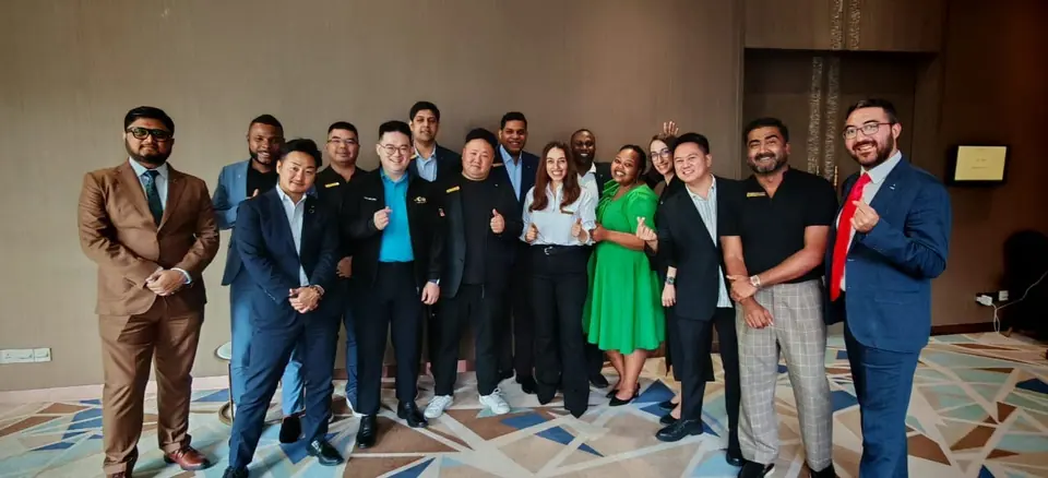 A group of about fifteen participants in suits and dresses posing for a group photo in a hotel hall