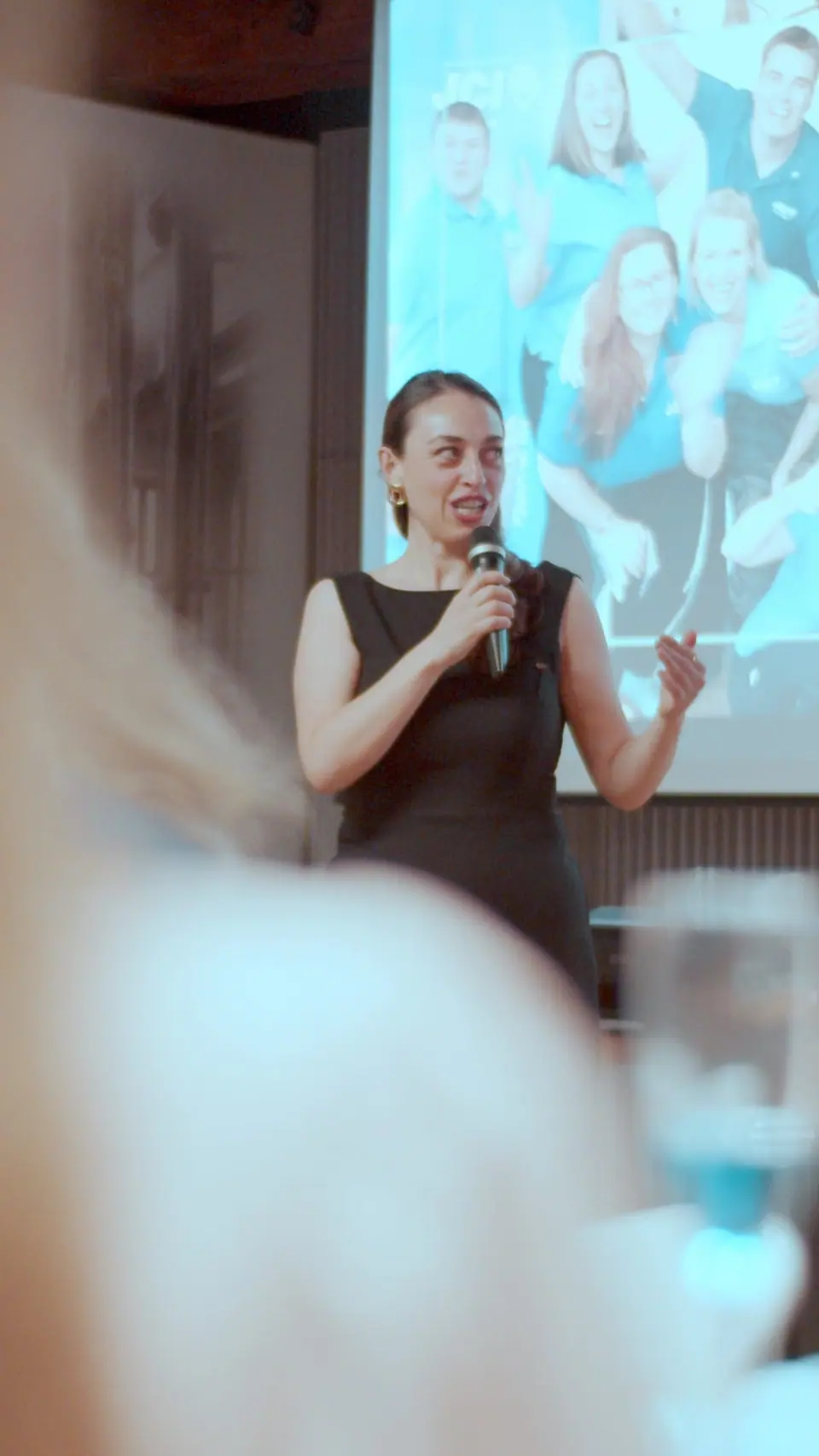 A woman with a microphone presenting in front of a projected team photo