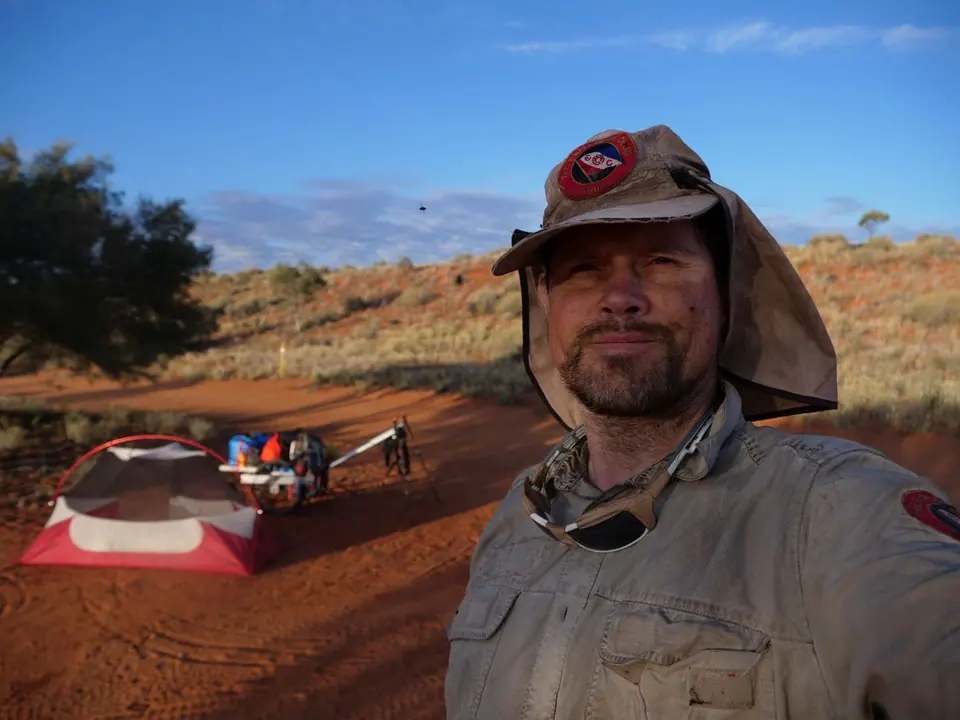 A man in a desert hat in front of his tent and cart in the outback