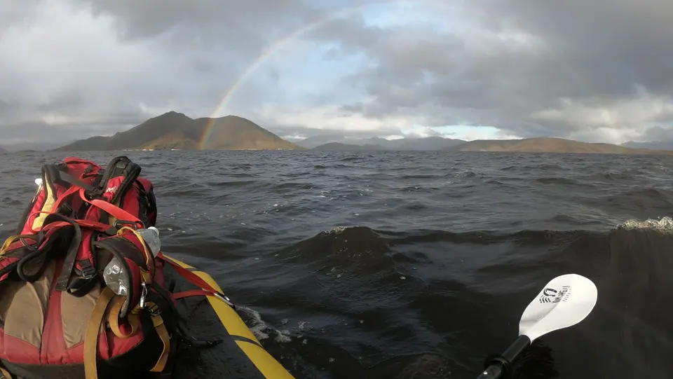 A kayak packed with gear on choppy water under a rainbow