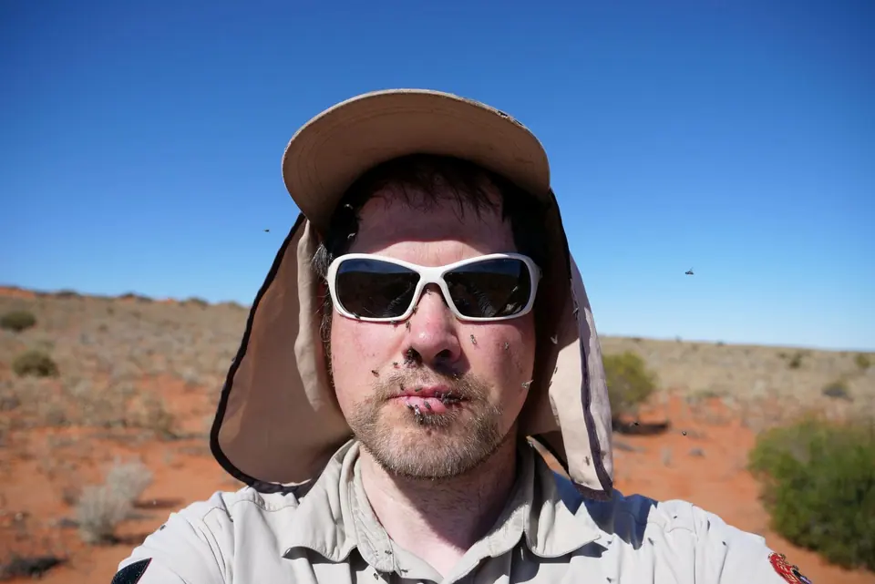 A man in a wide-brimmed sun hat and sunglasses taking a selfie in the desert