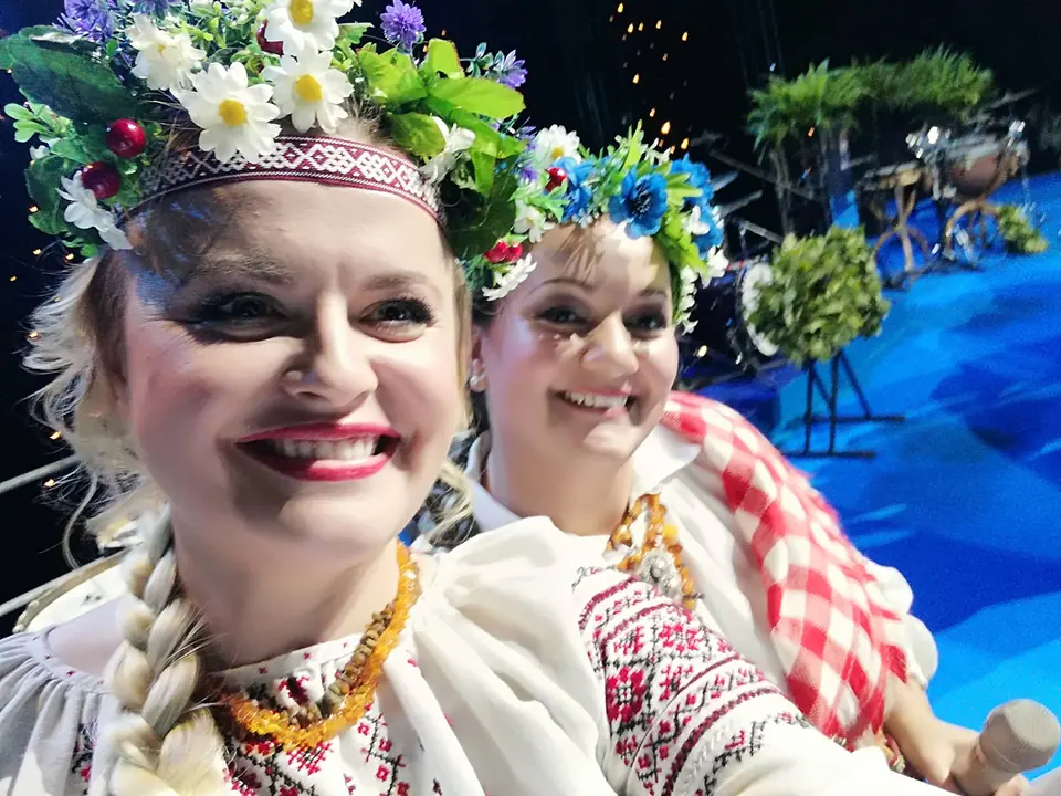 Two smiling women wearing flower crowns and traditional embroidered costumes