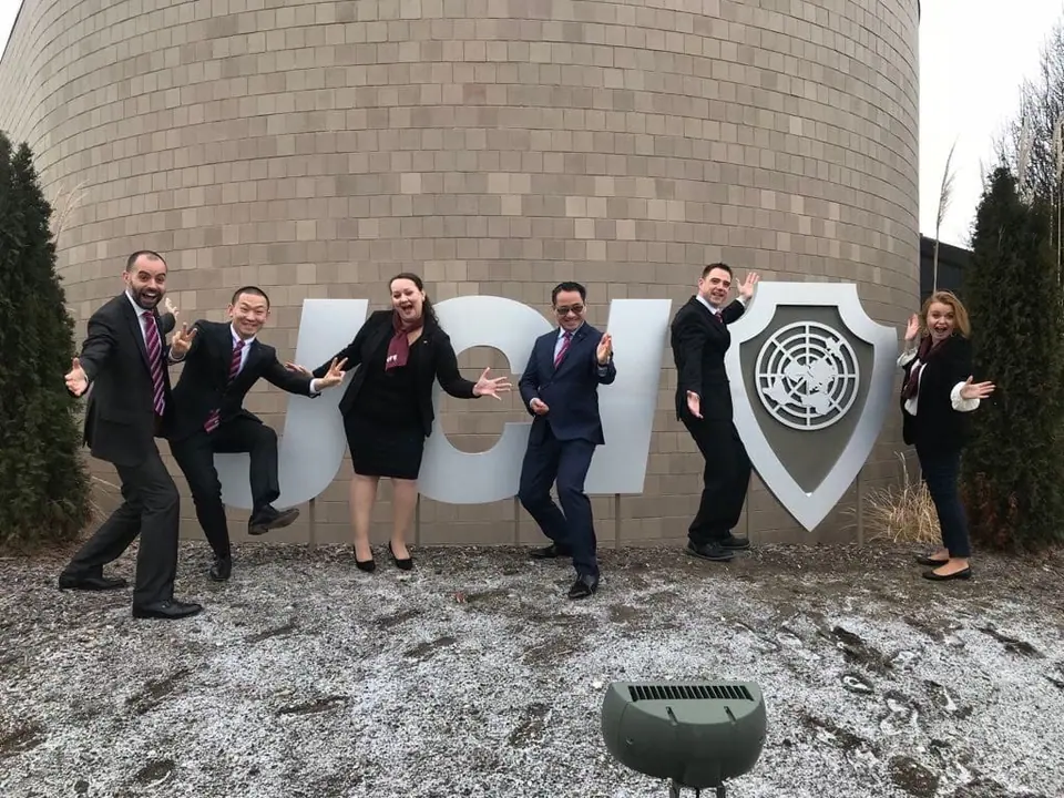 Six JCI members posing in front of a large JCI sign outdoors